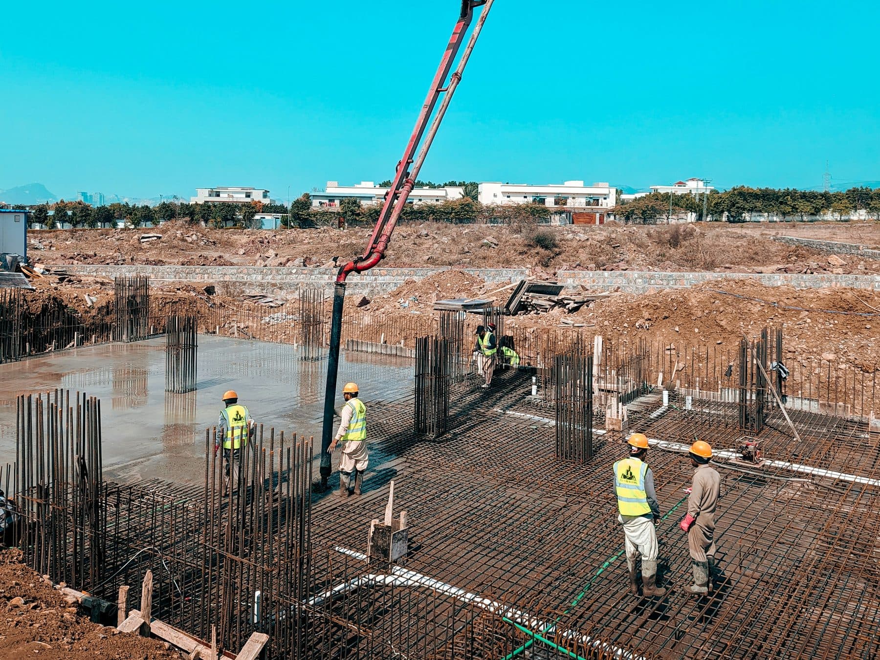 Site crew placing concrete across a reinforced foundation raft, with the pump boom feeding the pour.